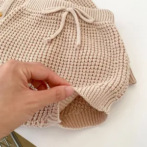 Detalle de pantalones de punto beige para bebé con textura acanalada y cordón en cintura