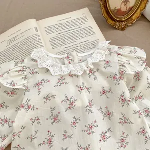 Dettaglio camicetta neonata a fiori con colletto in pizzo e maniche a sbuffo su libro