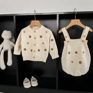 Détail d'un cardigan tricoté pour bébé avec broderie florale et barboteuse assortie