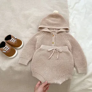 Detalle de conjunto de punto para bebé con textura waffle, botones de madera y pompón en capucha