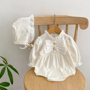 Detail eines weißen Baby-Stramplers mit großer Schleife, Perlenknöpfen und Rüschenbesatz