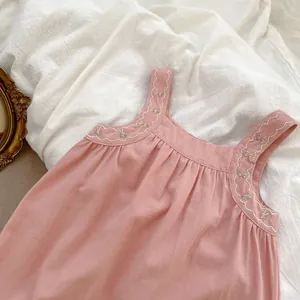Dettaglio della salopette rosa per neonata con ricami smerlati bianchi e motivi floreali
