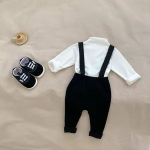 Flat lay of baby white mock neck top and black ribbed suspender trousers with shoes