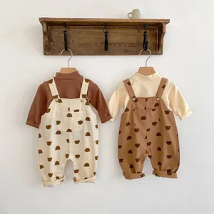 Detailansicht der Baby-Latzhose mit Bärenprint und Langarmshirts an Holzhaken