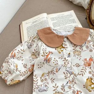 Detail of baby romper with forest animal print and brown Peter Pan collar on linen fabric