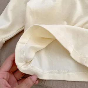 Detail of double-needle hem stitching on soft beige cotton baby long-sleeve bodysuit