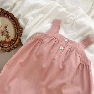 Dettaglio dell'abito con bretelle rosa per neonata con bottoni bianchi e pieghe