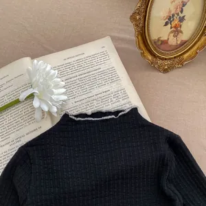Detail of baby girl black ribbed knit mock-neck top with ruffled collar and soft texture