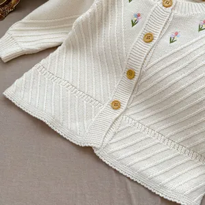 Detailaufnahme der cremefarbenen Strickjacke mit Blumenstickerei und Holzknöpfen