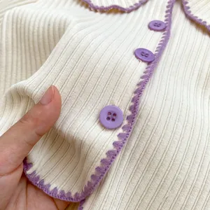 Detail eines cremeweißen Strick-Cardigans mit lila Knöpfen und gewelltem Saum