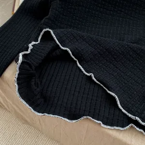 Macro detail of black ribbed knit fabric with delicate white ruffled lettuce edge stitching