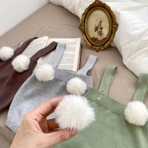 Dettaglio di pagliaccetti in maglia marrone, grigio e verde con decoro a pompon bianco