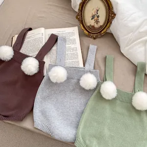 Dettaglio di pagliaccetti in maglia per neonati con pompon bianchi in marrone, grigio e verde