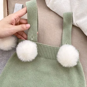 Dettaglio tutina neonato in maglia con pompon bianchi e texture verde morbida