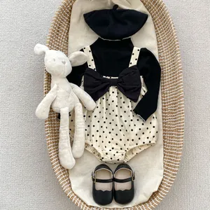 Flat lay of baby girl polka dot romper set with black top, beret, and bunny toy