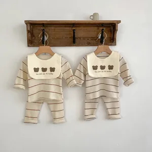 Détail de pyjamas rayés pour bébé avec bavoir ours brodé accrochés sur un support bois