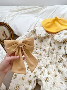 Detail of floral padded baby romper with yellow bow accessory on white bedding