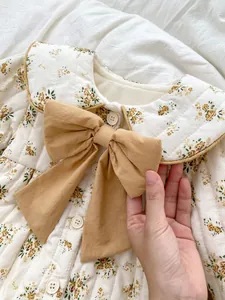 Detail of floral quilted baby romper featuring a mustard yellow bow and Peter Pan collar