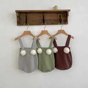 Dettaglio di tre pagliaccetti in maglia per neonati con pompon appesi a un gancio