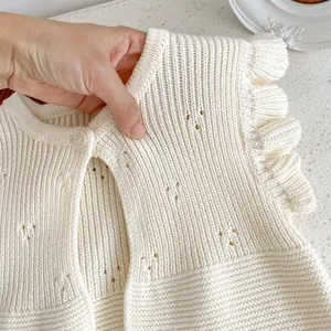 Sleeveless knitted baby cardigan in cream white with ruffle shoulders and hollow patterns