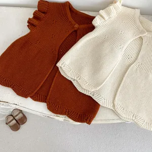 Detail of baby knit vests featuring ruffle sleeves and single-button closure in warm tones