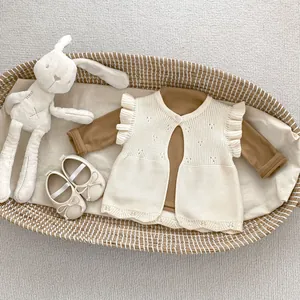 Detail of baby knit vest with ruffled sleeves and beige bow shoes in a woven basket