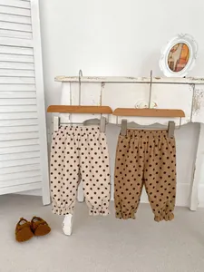 Detail of baby corduroy pants with polka dots and ruffled leg openings in warm tones