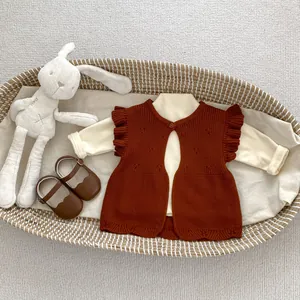 Flat lay of baby knit vest with ruffle sleeves and cream bodysuit in a basket