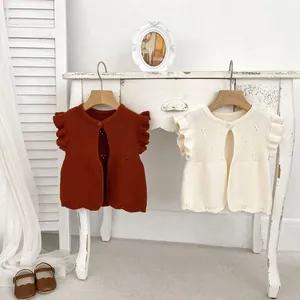 Detail of knitted baby vests in caramel and off-white with ruffle sleeves and wavy hems