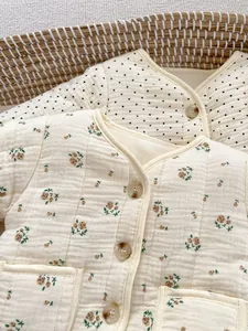 Detail von wattierten Babyjacken mit Blumen- und Punktmuster in einem Weidenkorb