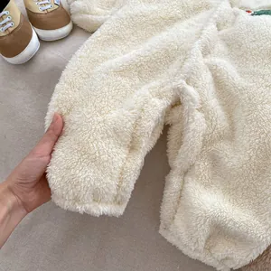 Close-up of soft white fleece baby romper featuring a cute green dinosaur embroidery detail