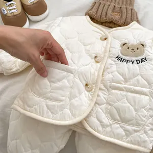 Detail of white quilted baby suit with cute bear embroidery and HAPPY DAY text
