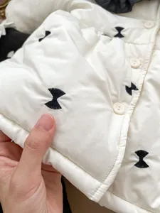 Close-up of thick white winter coat featuring black bow embroidery and round buttons