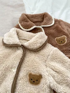 Dettaglio di tutine in velluto per neonati con ricamo a forma di orso e bottoni tondi