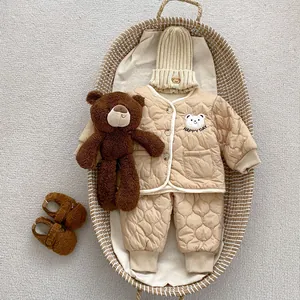 Flat lay of baby winter quilted set with bear embroidery and knit hat in woven basket
