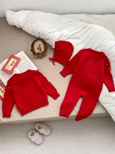 Detail of red knit baby bodysuit set with 3D white pom-poms and matching earflap hat