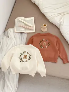 Detail van de schattige beerborduring op gebreide babytruien in beige en karamel