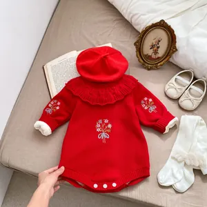 Détail d'une barboteuse en tricot pour bébé rouge avec broderie florale et col en dentelle