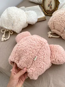 Detailed close-up of fuzzy teddy fleece bear ear hats in cream and soft pink colors
