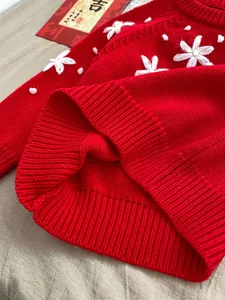Close-up of red knit baby romper featuring white flower embroidery and ribbed texture