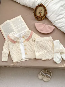 Détail du cardigan en tricot pour bébé avec motif losanges et bordure au crochet corail