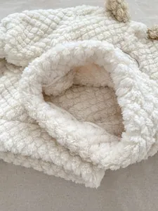 Close-up of white fleece baby winter set with honeycomb texture and brown pom-poms