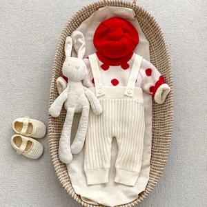 Ensemble bébé en tricot à pois rouges avec salopette et béret rouge dans un berceau