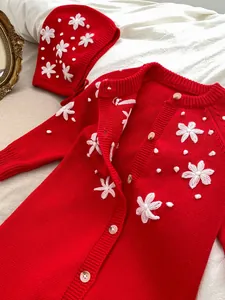Detail view of red knitted baby cardigan with white floral embroidery and matching hat set