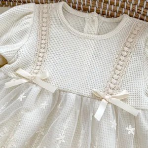 Detailed close-up of beige infant dress with waffle knit texture and floral embroidery mesh