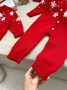 Detail of red knitted baby romper featuring 3D crochet flowers and pearl bead accents