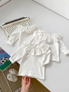 Detailed view of three white long-sleeved baby shirts with ruffled lace collars