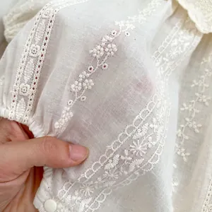 Close-up of intricate flower embroidery and lace hollow-out details on white baby blouse