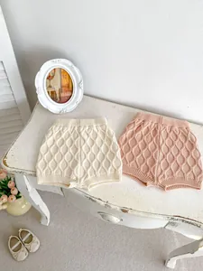 Détail de la texture tricotée à losanges sur les shorts bébé en coton crème et rose