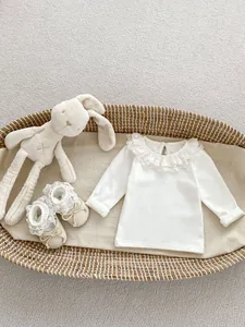 Detail of white cotton baby top with lace ruffle collar and matching bow shoes